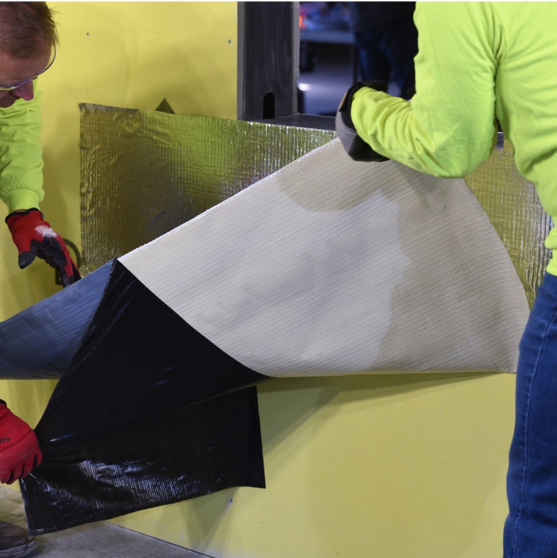 Application of reinforced aluminum butyl adhered AWB on a commercial building wall.