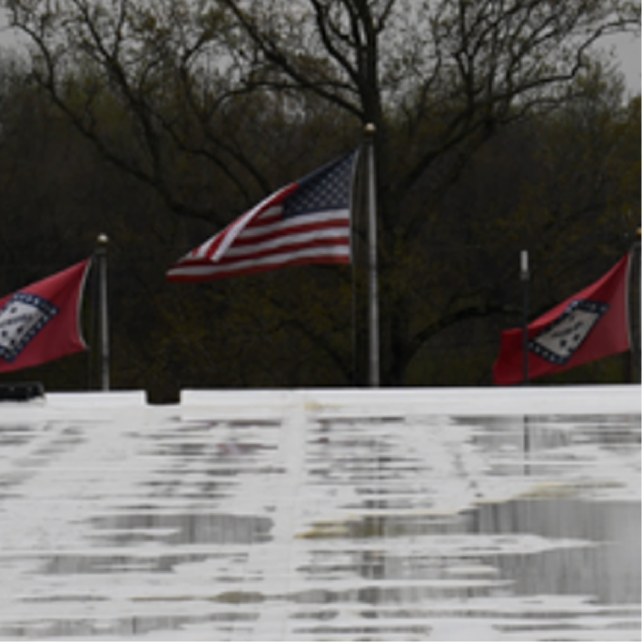 Arkansas state flags and the U.S. flag overlooking a commercial flat roof with standing water after rain.