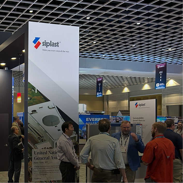 Industry professionals networking at a Siplast trade show exhibit booth during a commercial roofing conference.