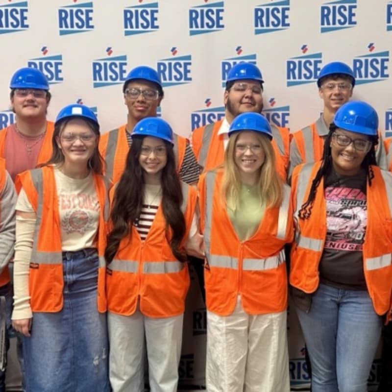 Arkadelphia High School students in hard hats and safety vests at Siplast RISE Center, learning about careers in research and manufacturing.