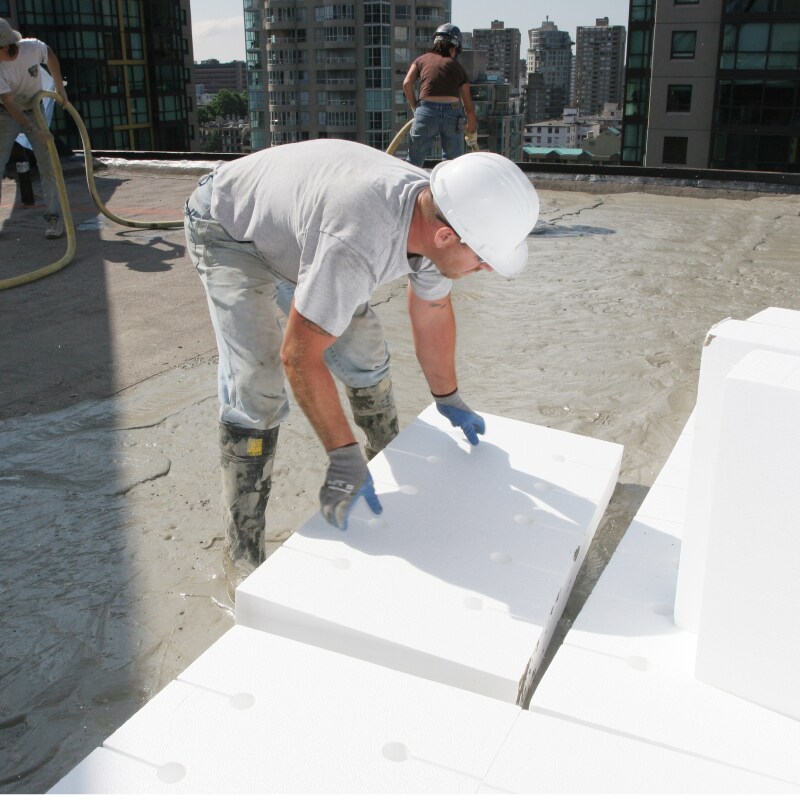Roofer installing EPS board into concrete slurry to dry overnight