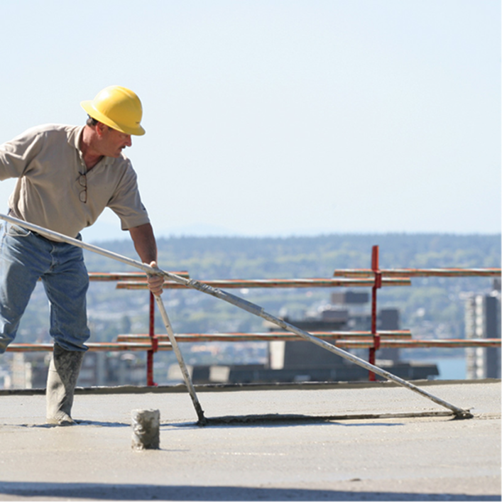Construction worker leveling lightweight insulating concrete (LWIC) over a roofing substrate.