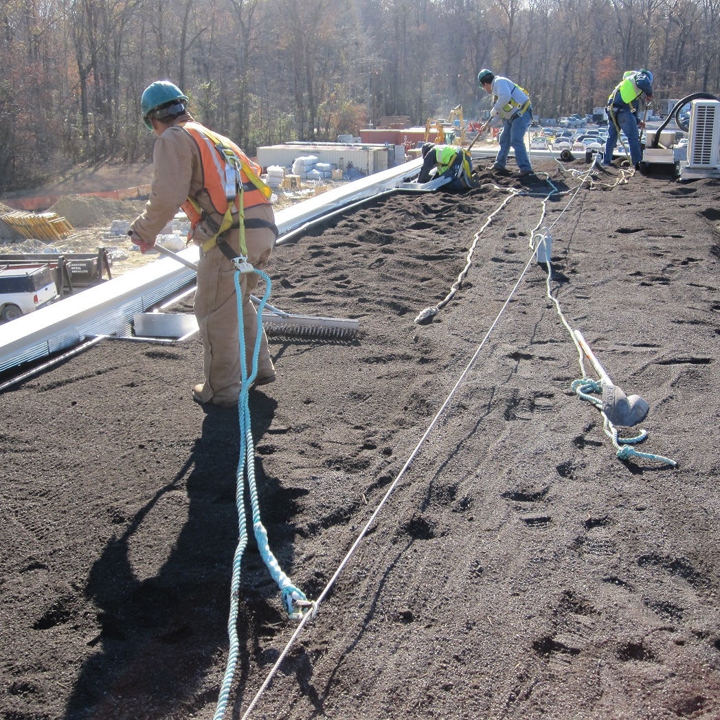 Construction workers on a rooftop installing a single-source overburden assembly, highlighting simplified jobsite coordination