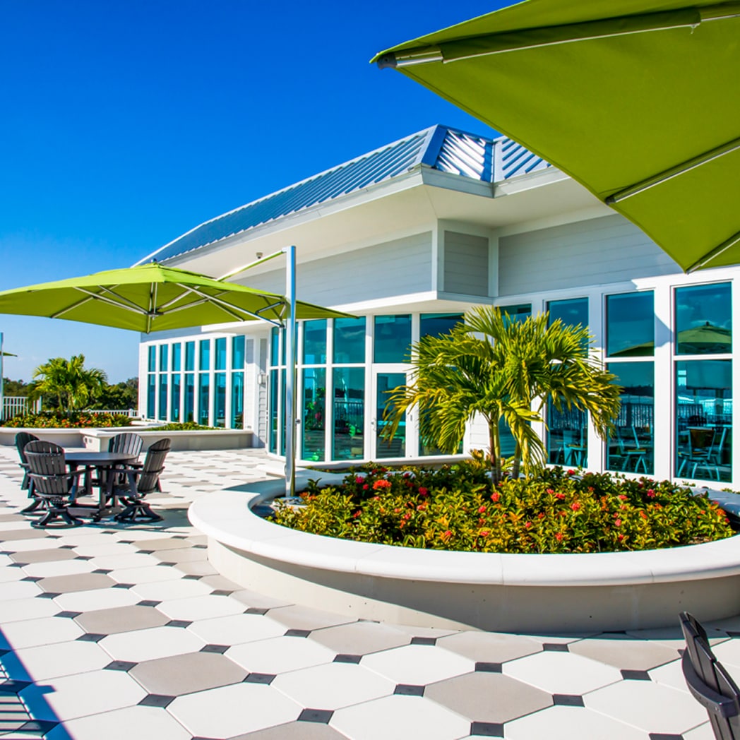 A bright outdoor patio features a patterned tile floor with umbrellas, dining tables and chairs