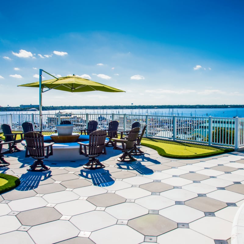 Rooftop amenity space with patterned pavers, lounge chairs, and umbrellas overlooking a body of water under a clear sky