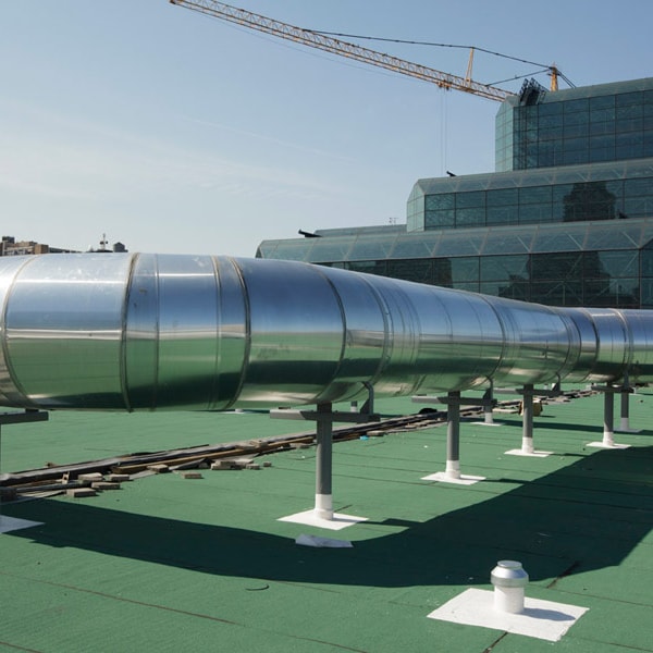 A medium shot captures large, cylindrical, metallic structures on a rooftop, highlighting a tailored engineering solution against a partly cloudy sky and a distant cityscape with a construction crane