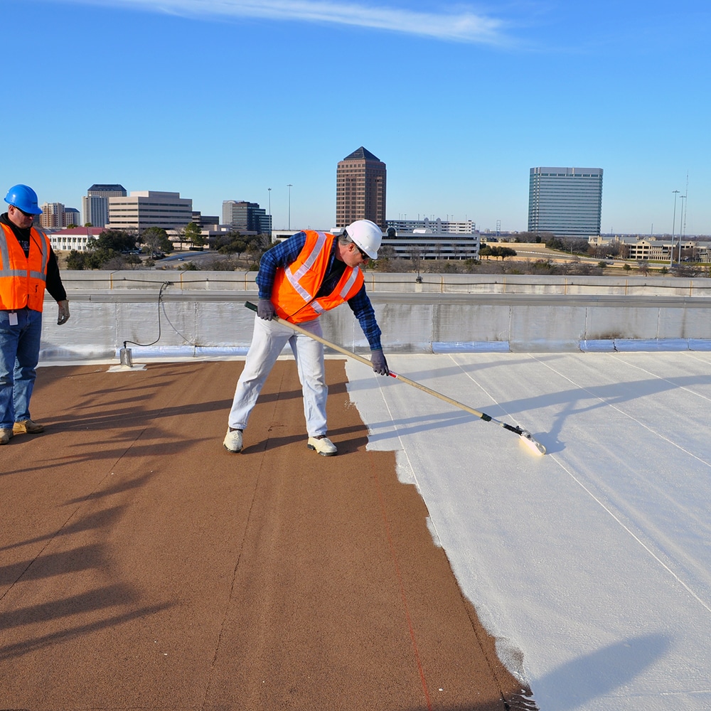 Commercial roofing contractor applying liquid-applied roof coating with a roller on a flat roof assembly.