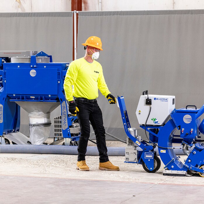 Contractor in high-vis gear uses a shot blaster, representing Contractor Resources like guides, specs, and data sheets.
