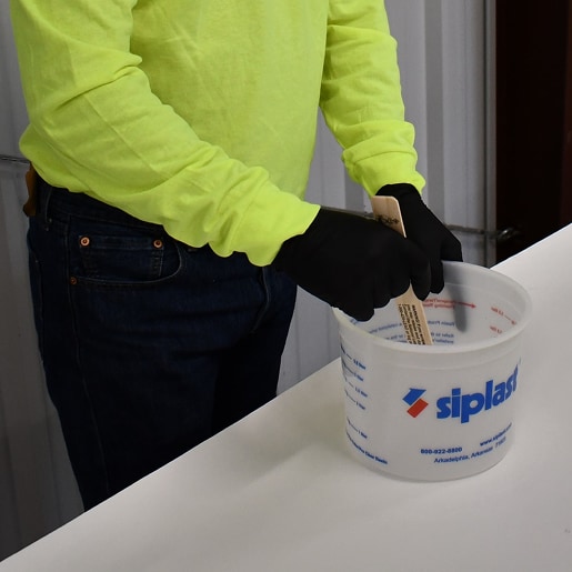 Contractor mixing liquid product in a Siplast bucket, representing Material Estimating Calculators for liquid applications.