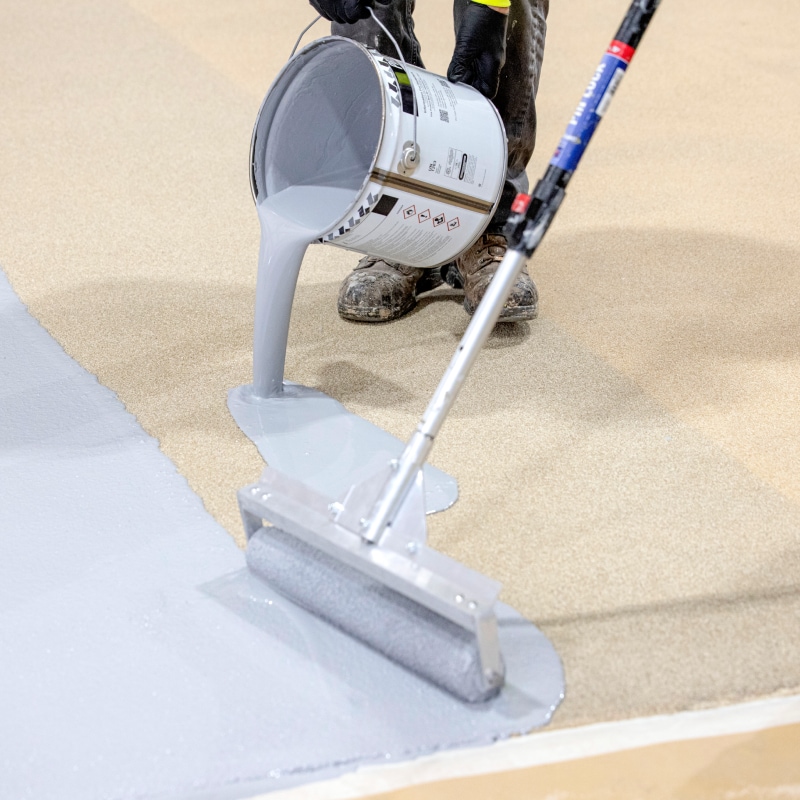 Worker pours liquid PMMA coating onto a deck, illustrating the webinar on Substrate Analysis and Preparation for traffic applications.