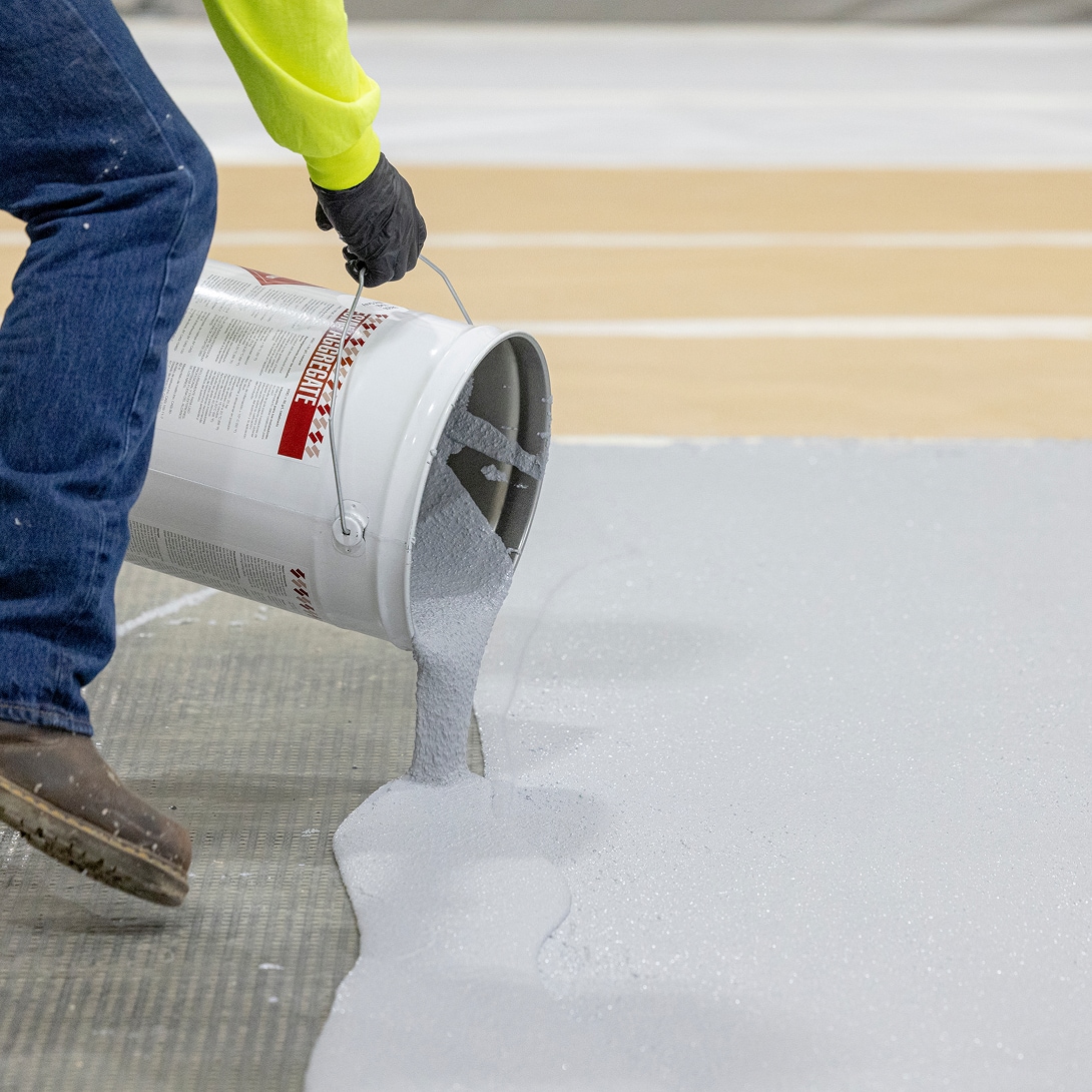 Construction worker pouring gray Terapro 220 or 250 concrete protection coating onto a floor for durable protection.