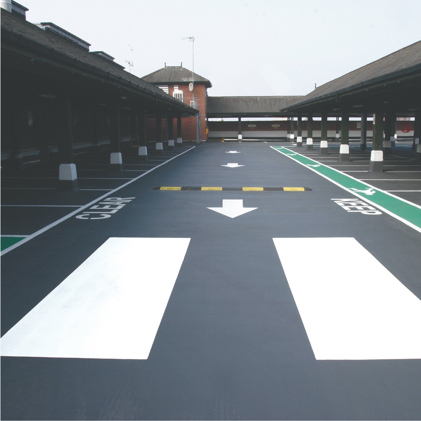 Freshly marked and coated surface of a parking facility, showing dark gray lanes, white arrows, and green painted sections.