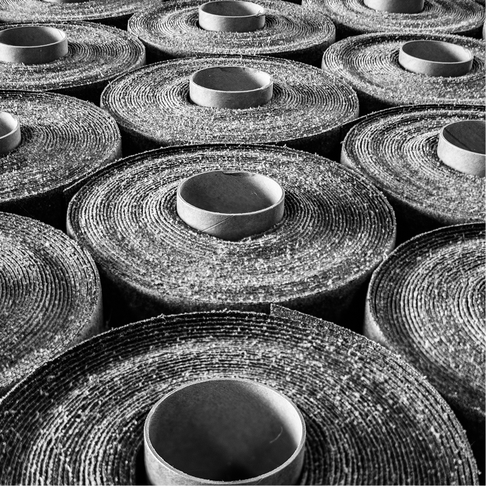 High-texture rolls of asphalt roofing underlayment stored in a warehouse, black and white industrial photography.