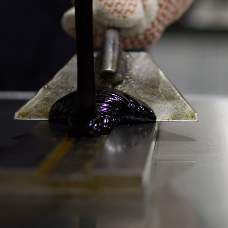 Thick, black modified-bitumen compound being applied, illustrating the composition of an SBS roofing membrane.