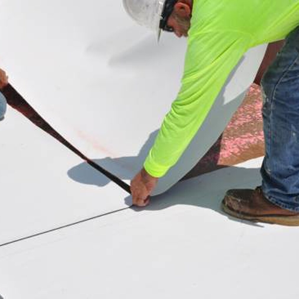An installer works on a seam of a white single-ply membrane, showcasing the precision and detail involved in roofing installation.