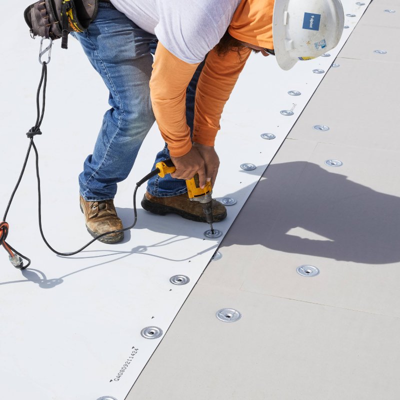 A contractor on a commercial rooftop installing Siplast roofing material with a drill, emphasizing Siplast's support and resources for contractors.