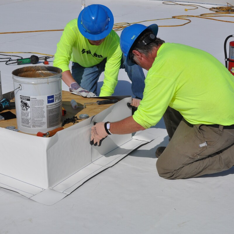 Roofers installing PVC roofing materials using fasteners, plates, and adhesives
