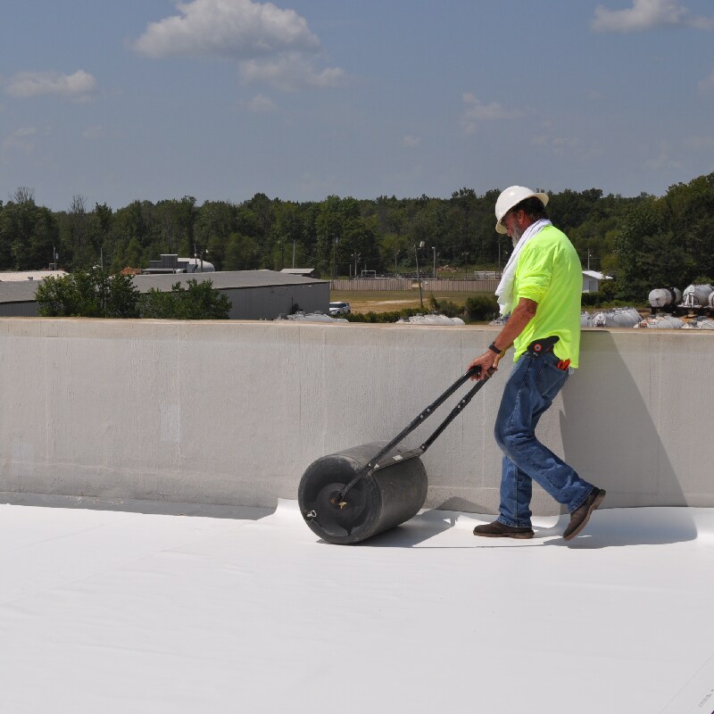 Roofer using large roller to install single-ply roof products by Siplast 