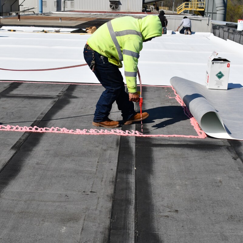 Roofer adding singe-ply roofing membrane on top of other materials