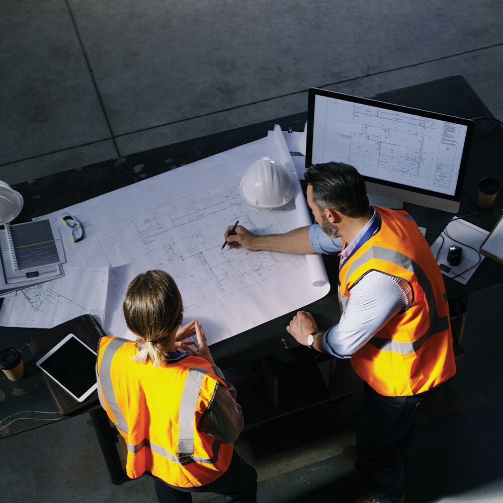 Two commercial building enclosure professionals examining architectural blueprints to bid on Siplast systems.