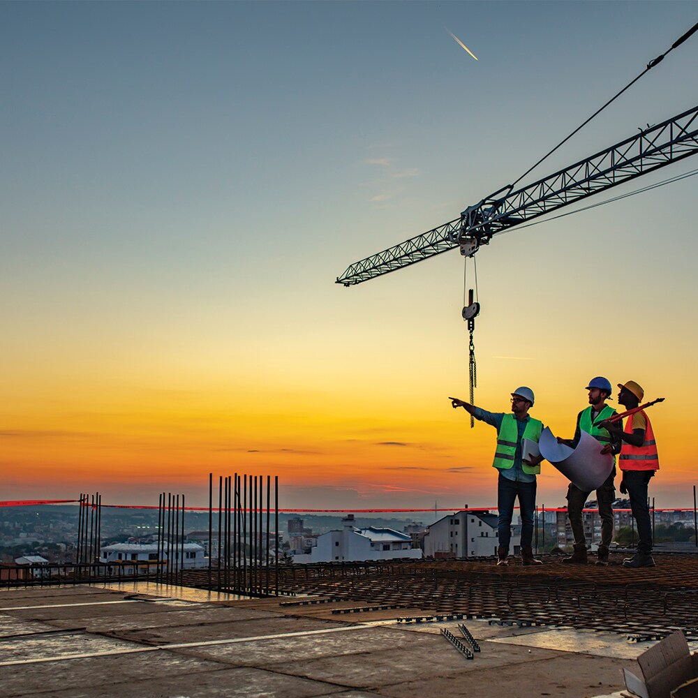 Construction engineers and contractors reviewing architectural blueprints on a commercial roof site at sunset.