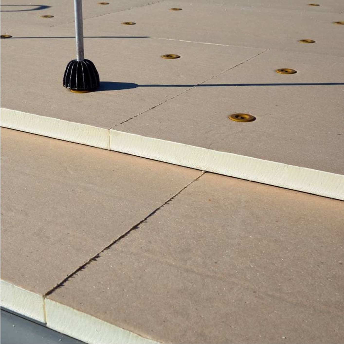 Close-up of beige rigid insulation boards laid on a commercial roof, with a single black fastener visible, ready for roofing membrane installation.