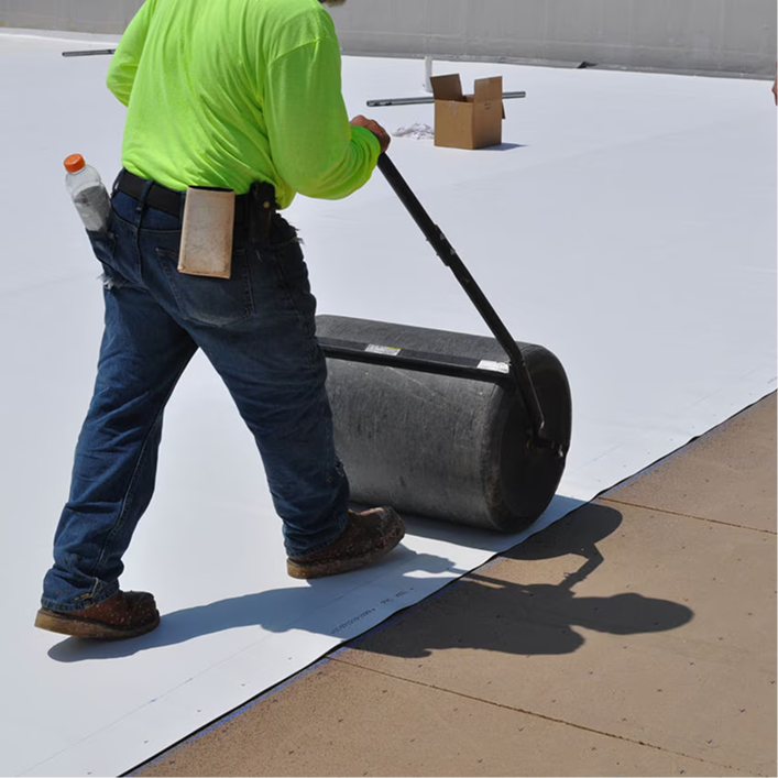 Roofing installer using a weighted roller to smooth out a low-slope membrane during installation.