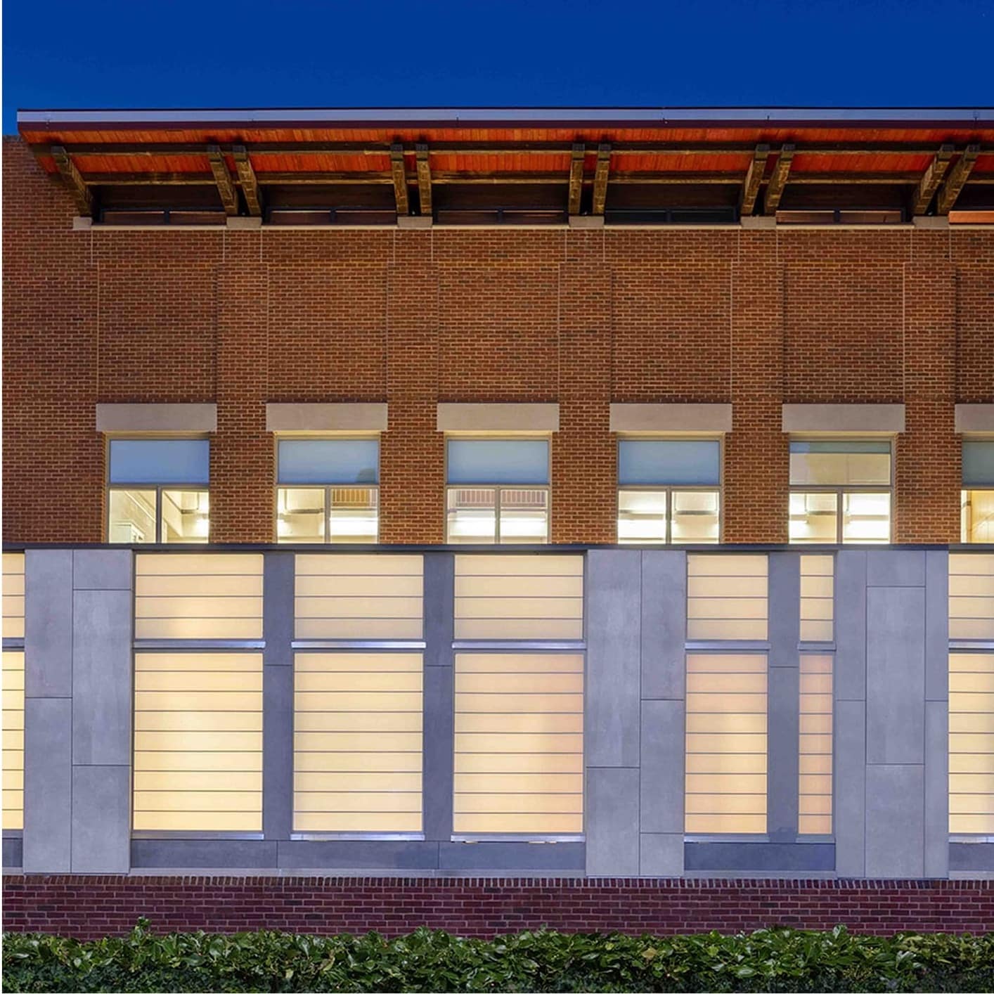 Modern brick building with a glowing translucent lower facade and an exposed wood and metal roof structure at dusk, highlighting architectural lighting and design for the Siplast RISE blog.