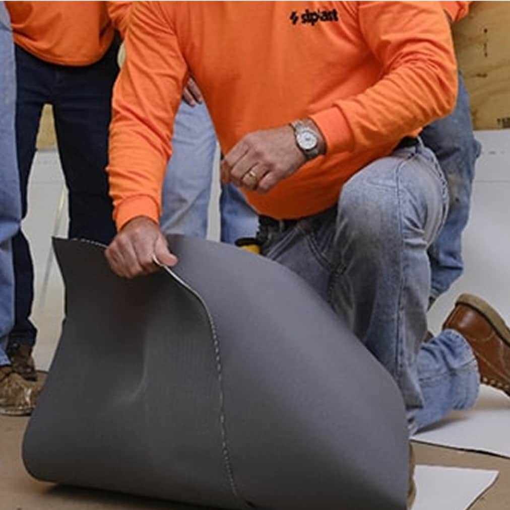 A Siplast roofing technician in an orange shirt demonstrates the flexibility and quality of a Siplast commercial roofing membrane to a group of onlookers, emphasizing the durable materials used in Siplast roofing and waterproofing systems.