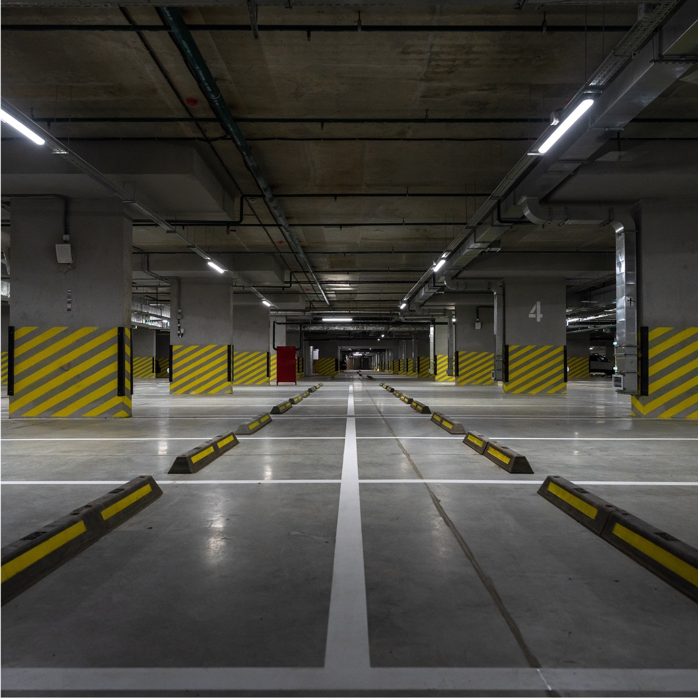 Empty underground parking garage with yellow and black striped safety barriers and exposed ceiling pipes, suitable for parking lot coatings and maintenance.