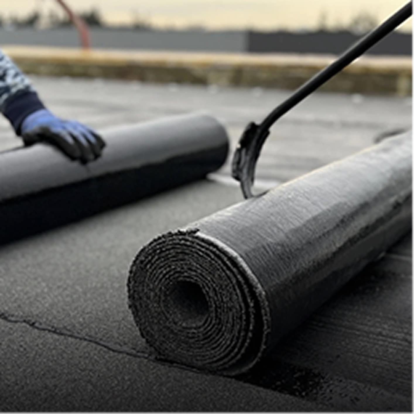 Black roofing rolls being installed on a flat roof with tar, ideal for commercial or industrial flat roof repair and waterproofing.