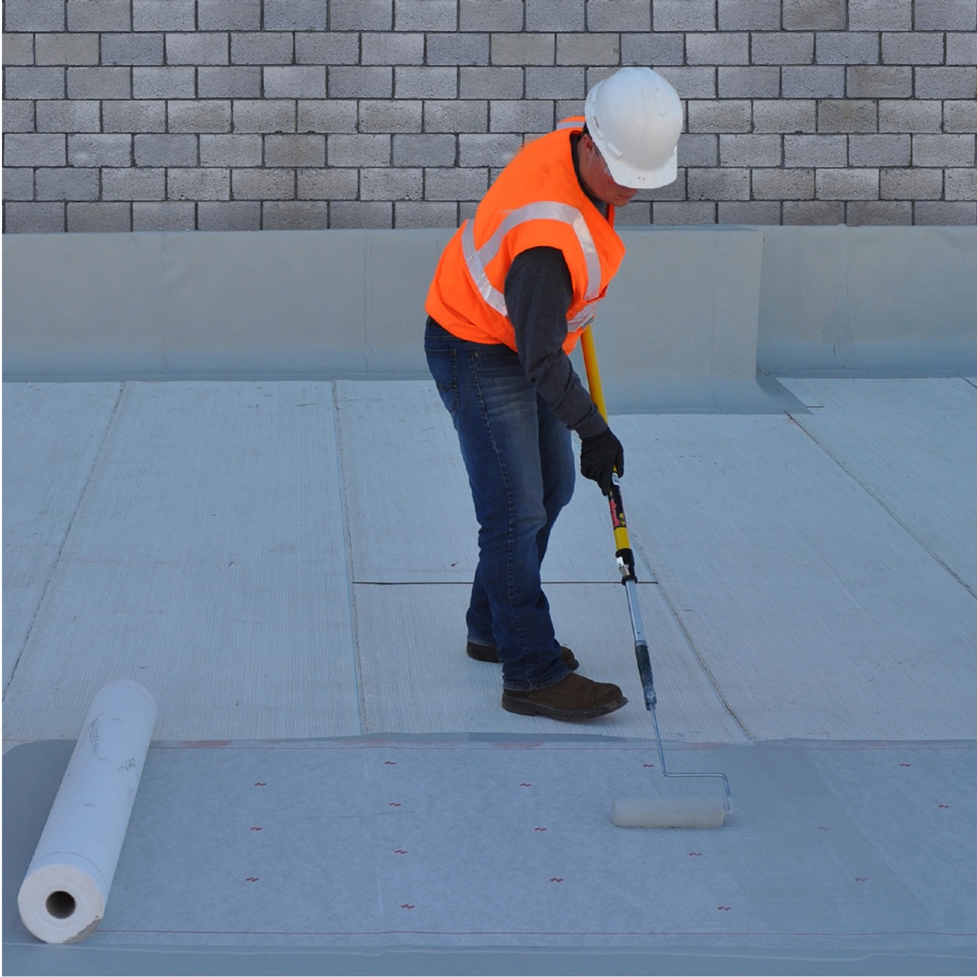 Construction worker installing a large roll of grey roofing membrane on a flat roof, demonstrating commercial roofing installation techniques.