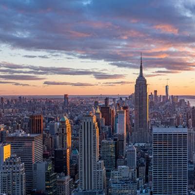 A panoramic view of the iconic New York City skyline at dusk, featuring the Empire State Building and other prominent skyscrapers, symbolizing the vast commercial properties that benefit from Siplast roofing and waterproofing guarantees and reliable systems.