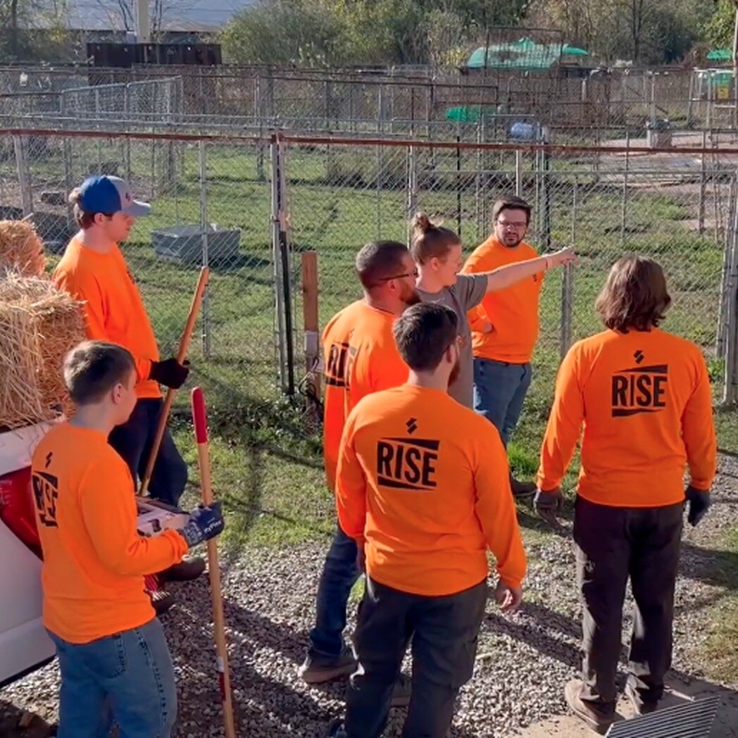 Siplast RISE Center employees in 'RISE' shirts volunteer at Clark County Humane Society, engaging in outdoor activities with animals.