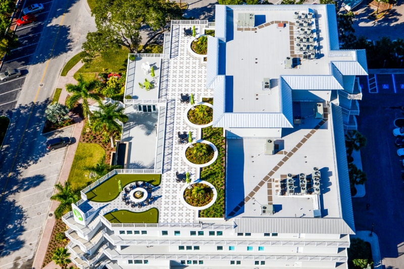 Aerial view of the modern IWG Riverside building rooftop amenity deck, featuring a putting green, circular planters with lush vegetation, seating areas, and rooftop mechanical equipment.