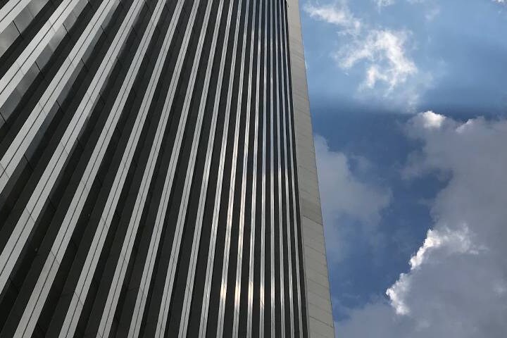 A modern skyscraper's vertical cladding or facade against a bright blue sky with white clouds.