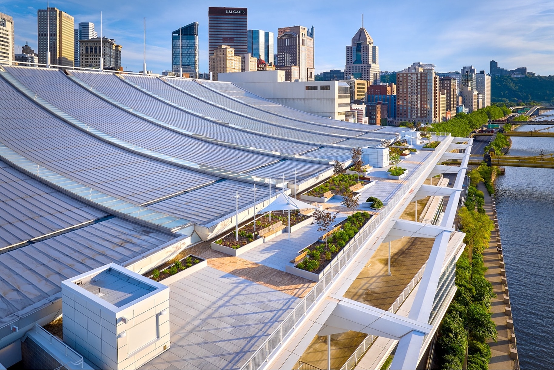 Panoramic view of the David L. Lawrence Convention Center in Pittsburgh, showcasing its expansive, undulating metal roof with green roof sections, overlooking the city skyline and river.