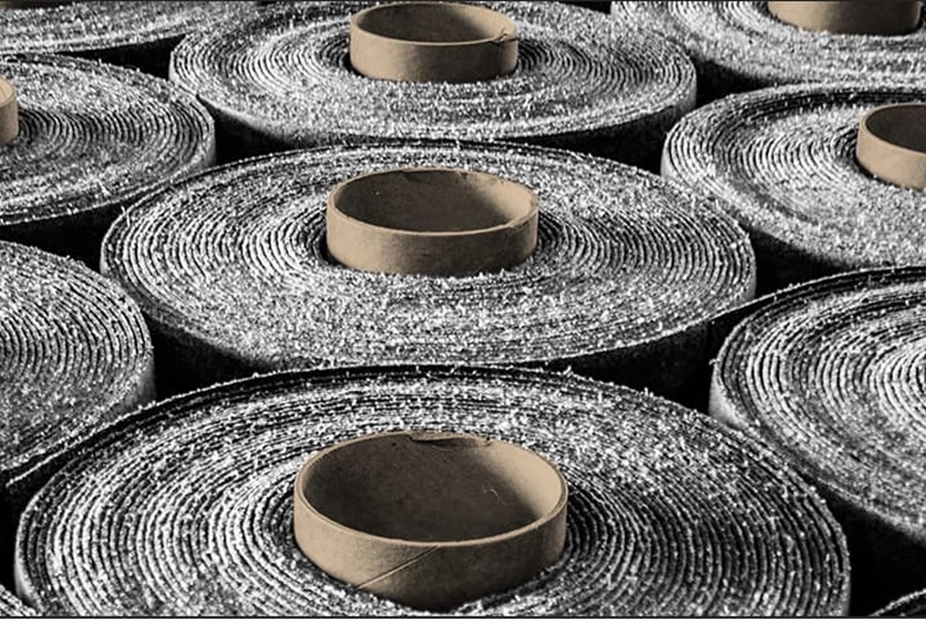Rows of rolled roofing membrane, possibly modified bitumen or asphalt, showcasing the textured surface and circular brown cores, ready for distribution or installation.