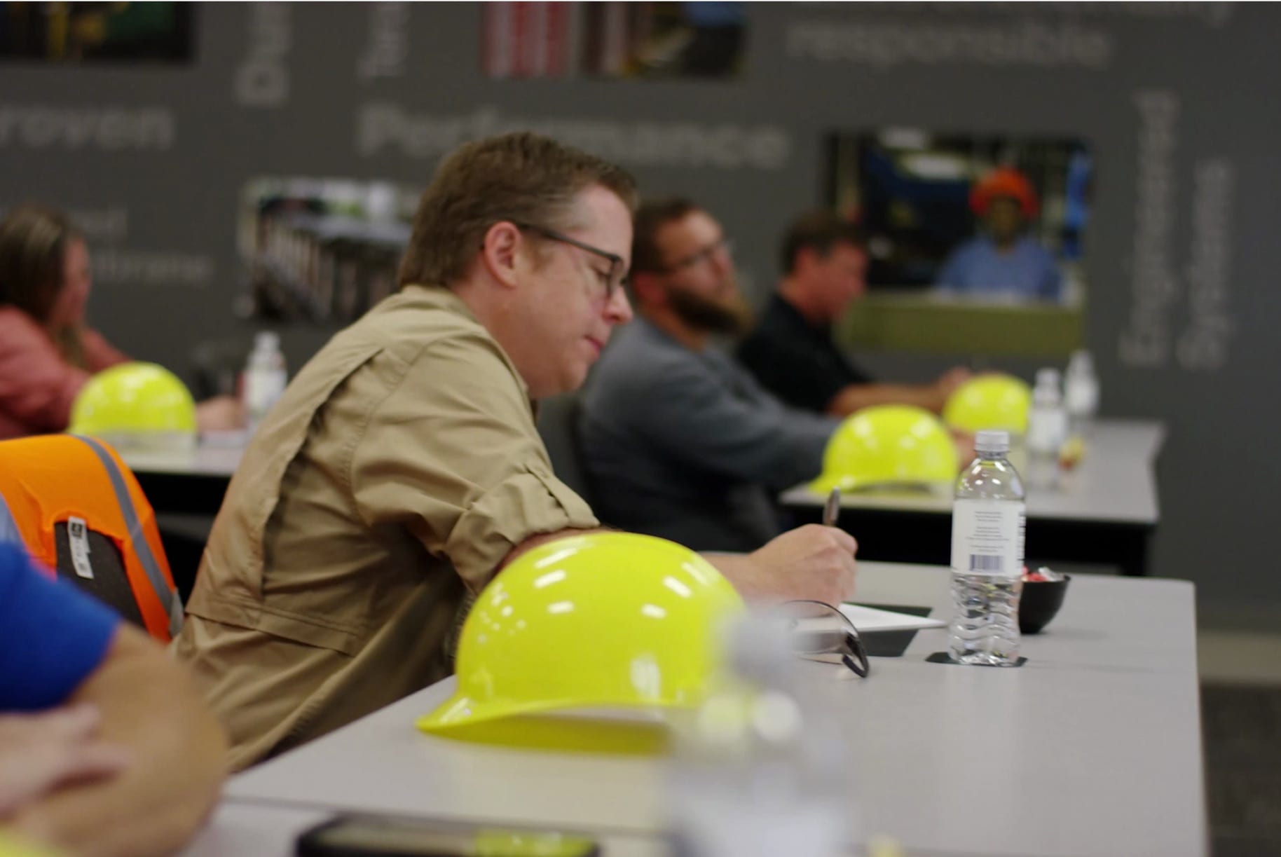 Attendees in a training session, with yellow hard hats on the table, listening to an instructor, representing the 'RISE on the Road' educational program.