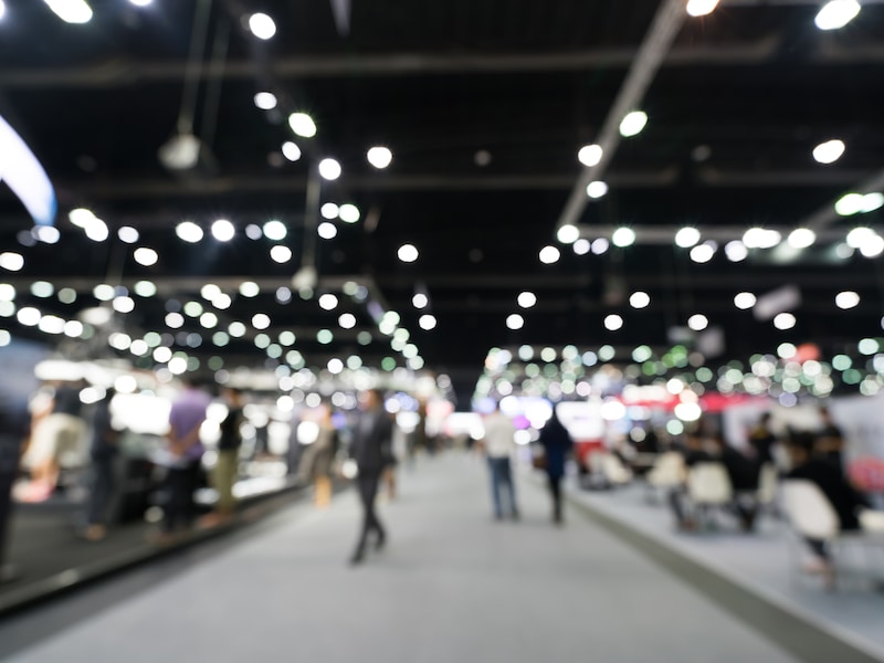 Blurred photo of a trade show floor, representing GAF and Siplast's collaborative building science and roofing events.