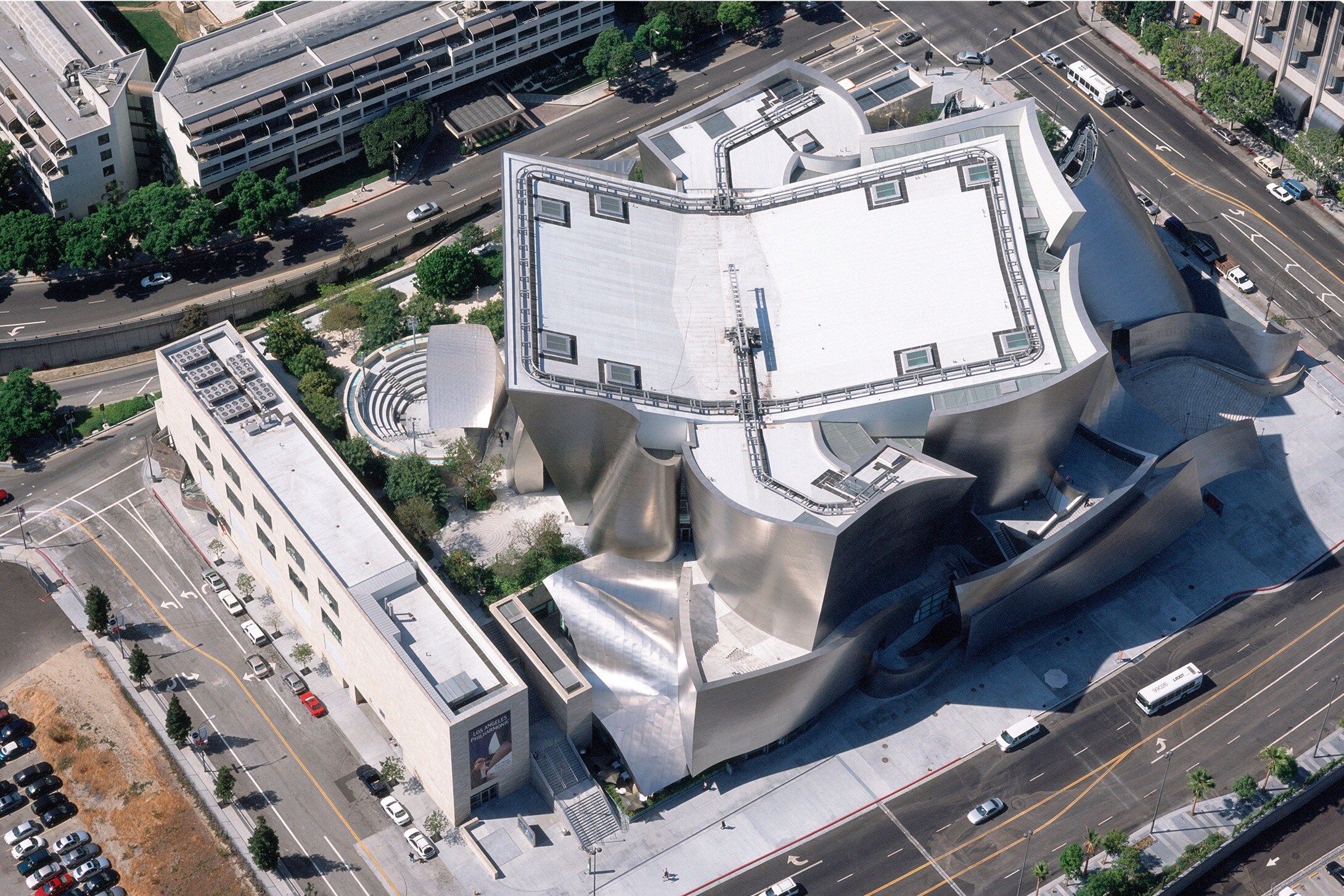 Aerial view of a unique modern concert hall with a wavy metallic facade and a distinctive white roof in an urban setting.