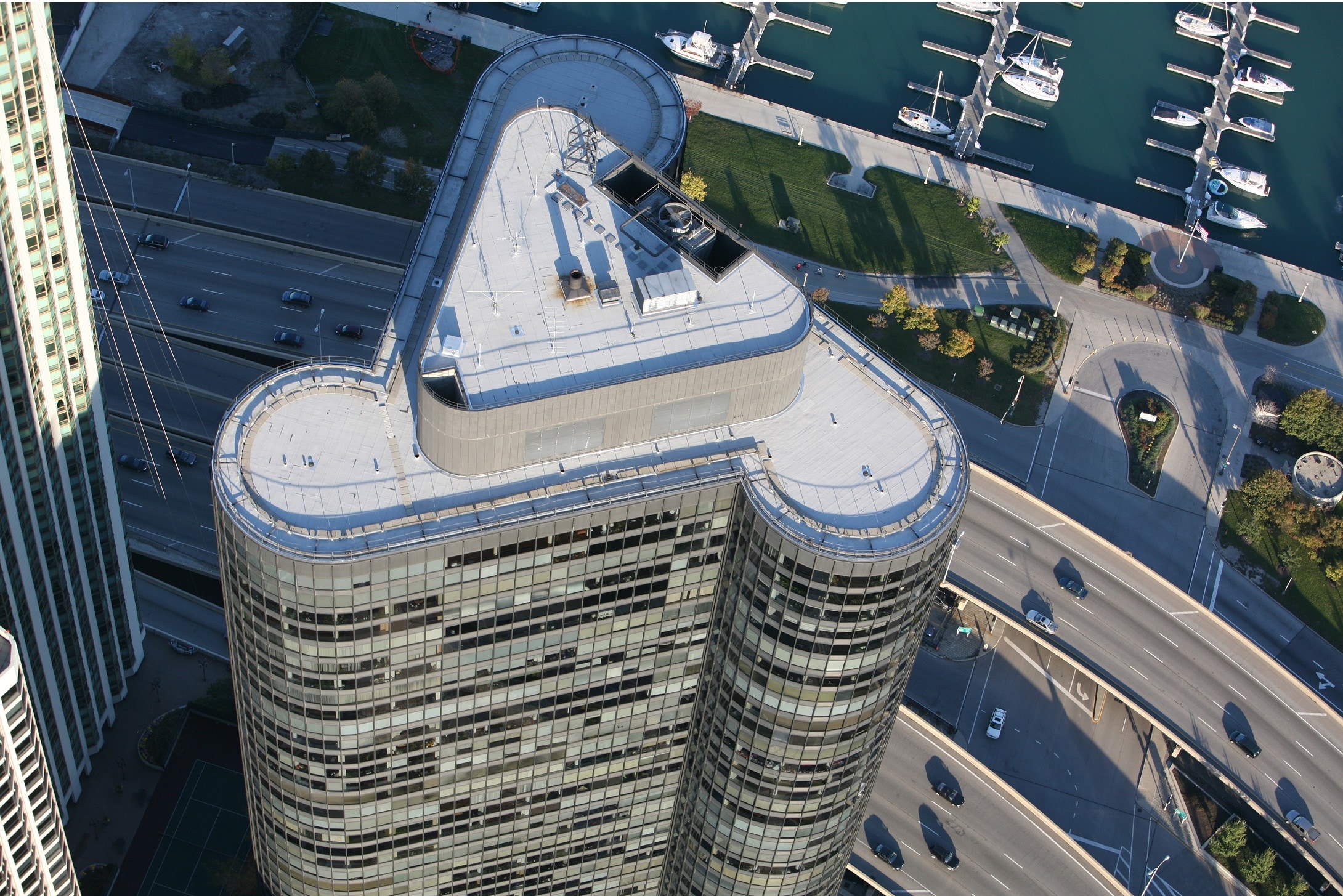 Aerial view of the uniquely curved Harbor Point building, situated next to a highway and overlooking a marina.