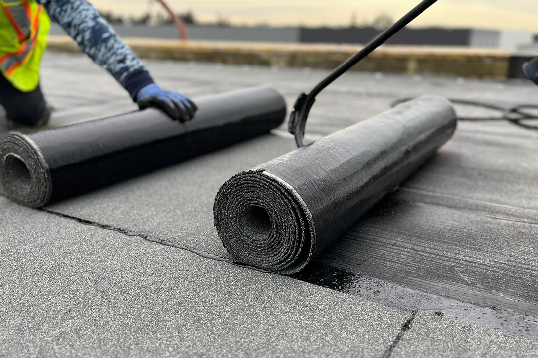 Professional roofers applying SBS rolled roofing using a torch-down method on a commercial flat roof.