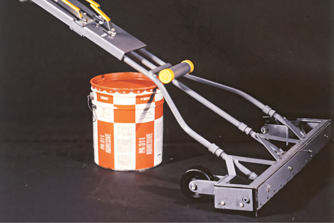 Specialized rolling applicator tool and bucket of PA-311 adhesive for controlled application of roofing materials.