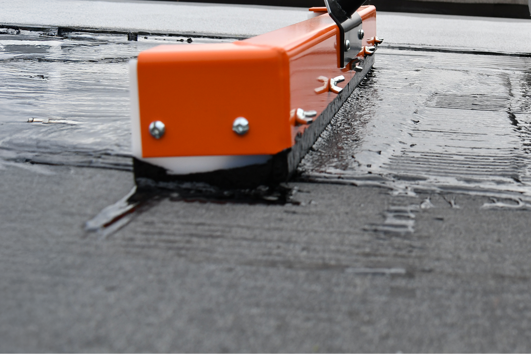 Close-up of a worker applying hot asphalt mopping for roofing, ensuring proper embedment in cool weather.