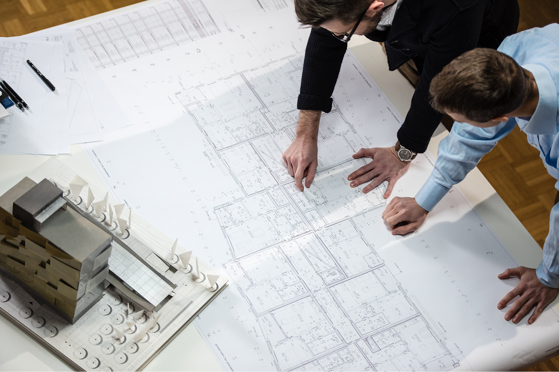 Construction specialists reviewing architectural blueprints and building models for complex project planning.