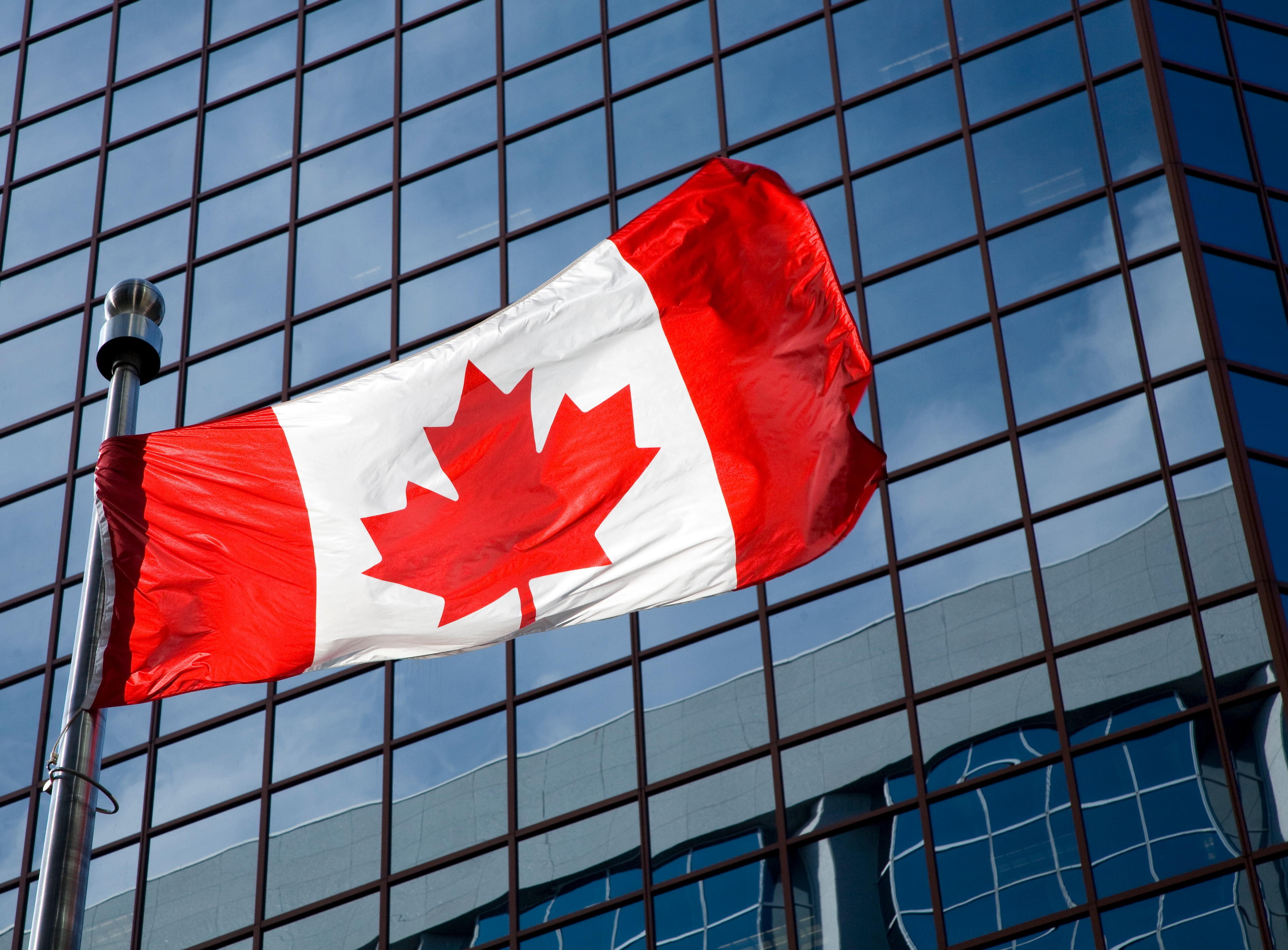Close-up of the Canadian maple leaf flag blowing in the wind, with modern building enclosure architecture in the background.