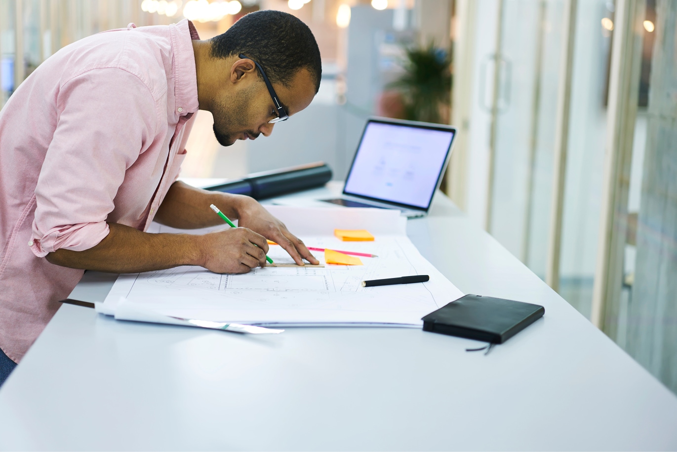 Commercial design professional reviewing architectural blueprints at a desk with a laptop, notebook, and drafting tools.