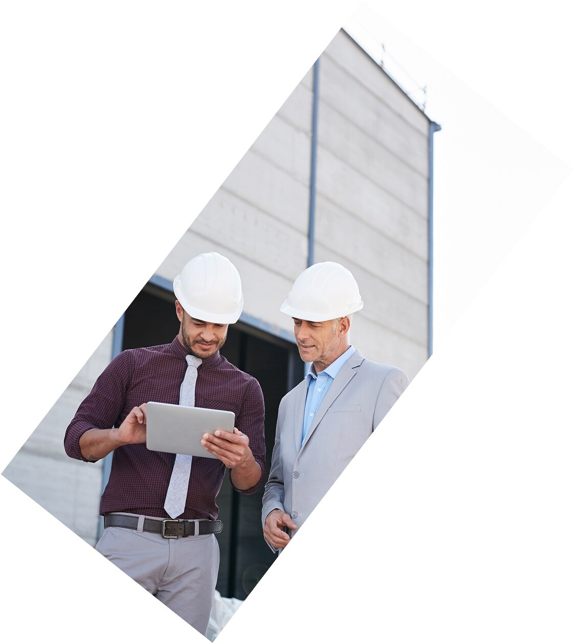 Two men wearing white safety helmets stand in front of a modern exterior wall system.