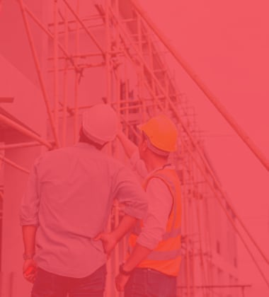 Red-toned stock photo of two construction workers in hard hats and safety vests discussing a project on a scaffolding backdrop.